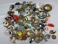 Overview of multiple costume jewelry pieces spread on a white surface. Includes earrings, pendants, pins, bracelets, and beads in various colors and materials.