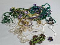Top view of assorted Mardi Gras bead necklaces tangled together with green and brown flip-flop sandals decorated with beads and a flower charm