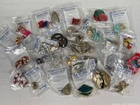 Photo showing multiple costume jewelry items, mostly earrings and pins, in small clear plastic bags.