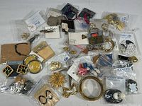 Wide angle view of assorted costume jewelry including earrings and pins in mostly gold and silver tones, packaged and loose.