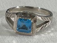 Front view of the ring showing the square-cut blue topaz stone and engraved pattern on the silver band.