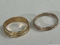 Two gold bands side by side, one yellow and one white, showing the ridged and textured design on the outer surface.