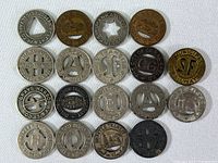 Full view of 18 vintage bus tokens arranged in rows showing various designs and cutouts from multiple U.S. cities.