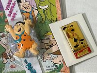 Close-up photo showing the Fred Flintstone watch figure and the Coca Cola World Cup pin side by side.