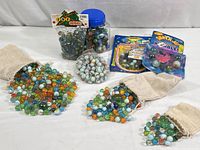 Overview of lot including plastic jar, three cloth bags of marbles, and sealed marble sets