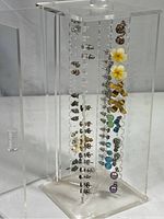Clear acrylic rotating display stand with stud earrings arranged vertically, showcasing variety and quantity.