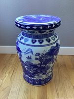 Front and side view of ceramic stand with blue and white painted waterfront village scene featuring houses, trees, and sailing boats.