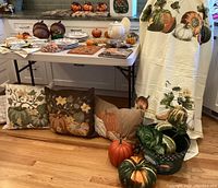 Overview of fall throw pillows, table linens, decorative pumpkins, and turkey-themed tablecloth on display in kitchen