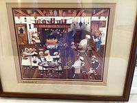 Framed signed print titled 'Bakers Baking' depicting bakers working in a kitchen with open fire.