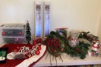Full lot display showing tree skirt, garlands, candle holder, assorted ornaments, Santa figurine, faux trees, and storage bins with greenery and ornaments.