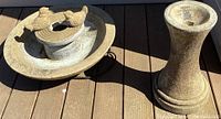 Overall view of the two concrete birdbath pieces placed next to each other on a wood deck surface.
