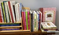 Wide view of multiple cookbooks including Barefoot Contessa, Susan Branch, Ina Garten and others, arranged on wooden shelf