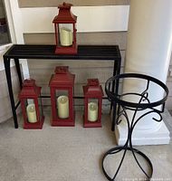 Overview of black metal plant stands with four red votive candle lanterns containing white battery-operated candles.
