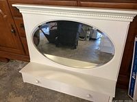 Front view of the white wall mount entry shelf with oval mirror and hooks showing overall structure and design.