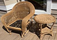 Front view of natural wicker gliding chair and matching wicker table on wooden deck