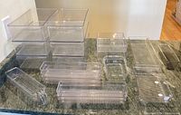 Clear plastic organizers arranged on countertop showing different shapes and sizes including stackable bins and trays with ridged bottoms.