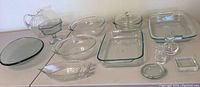 Photo showing all glass serving ware and Pyrex baking dishes arranged on table including large clear Pyrex baking dishes and various clear glass serving pieces.