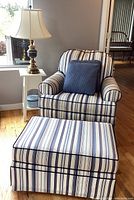 Striped upholstered armchair with matching ottoman, white side table, blue and gold lamp, and pillows from front angle