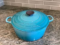 Turquoise enameled Le Creuset pot with lid on countertop, side view showing handles and pot shape.