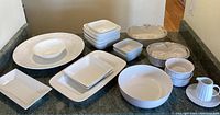 Wide view of all white dishes including plates, bowls, rectangular and square serving platters, and two Corningware lidded baking dishes.