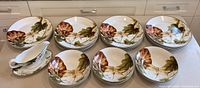 Wide shot of all 15 dinner plates, 6 bowls and gravy boat with underplate arranged on countertop