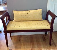Front view of wooden bench with yellow upholstery and back pillow showing curved armrests and floral pattern.