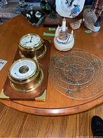 Wood plaque on table showing two brass instrument housings and wire basket at right
