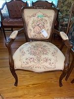 Front view of the antique Queen Anne armchair showing carved wooden frame, upholstery with floral and romantic tapestry.