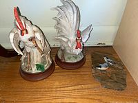 Two ceramic chicken figurines with red combs and wattles on wooden bases, and a painted bird artwork on Unakite stone with two White Breasted Nuthatch birds, signed by Joan A.