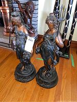 Front view of both statues side by side on hardwood floor showing full figures and bases
