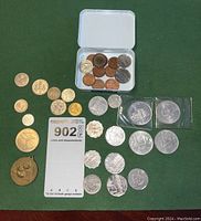 Top level view of all coins laid out on green cloth, with silver and copper coins visible, some in a small white box.