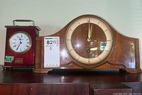 Photo showing German Forestville wooden mantle clock with rounded top and a Howard Miller Pepsi clock side-by-side on a shelf.