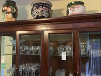 Wooden cabinet displaying multiple pieces of crystal glassware including brandy glasses and other clear glassware items
