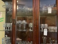 Crystal pinwheel glasses displayed inside a wooden and glass cabinet, including various stemware types set on glass shelves.