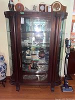 Front view of curved wood frame china cabinet with glass doors and shelves, containing various glassware and decorative items (not included).