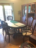 Wide view of oval pedestal dining table with two 18-inch leaves and six matching caned back armchairs with upholstered seats in dining room setting.