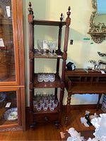 Full view of wooden open shelving display cabinet showing four shelves filled with glassware (excluded) and bottom drawer on caster wheels