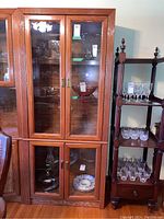 Full frontal view of wood display cabinet showing the upper and lower glass doors and shelves with glassware inside.