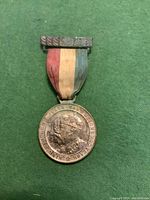 Front side of 1935 King George V Silver Jubilee medal featuring King George V bust and attached tricolor ribbon.