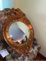 Full view of the gold framed round mirror resting on a patterned upholstered chair