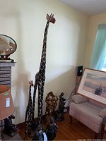 Three wooden giraffe statues of varying sizes grouped together next to a fireplace and couch.