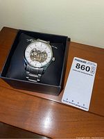 Kenneth Cole silver band watch in box with visible mechanical skeleton dial.