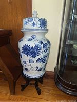 Full view of large blue and white floral ginger jar on wooden stand with lid.