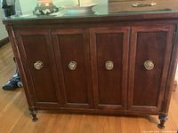 Front view of the mahogany sideboard showing four paneled doors with round brass knobs and glass top.