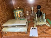 Photo showing marble jewelry box, cast metal napkin holder, three vintage perfume bottles, and English tea tin on a wooden surface.