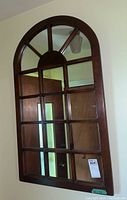 Arched wood frame mirror with windowpane design hanging on beige wall reflecting door and ceiling light.