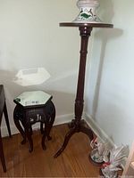 View of wooden pedestal stand with round top beside hexagonal mirror top side table, showing overall shape and size