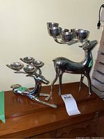 Two pewter deer candle holders displayed on wooden furniture, showing both standing and reclining deer.