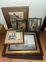 Photo showing five framed prints stacked together against a wall, featuring nautical, nature, and angelic themes.