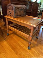 Wood side table with turned legs, slatted lower shelf, and wood keepsake chest on top, showing general condition and finish.